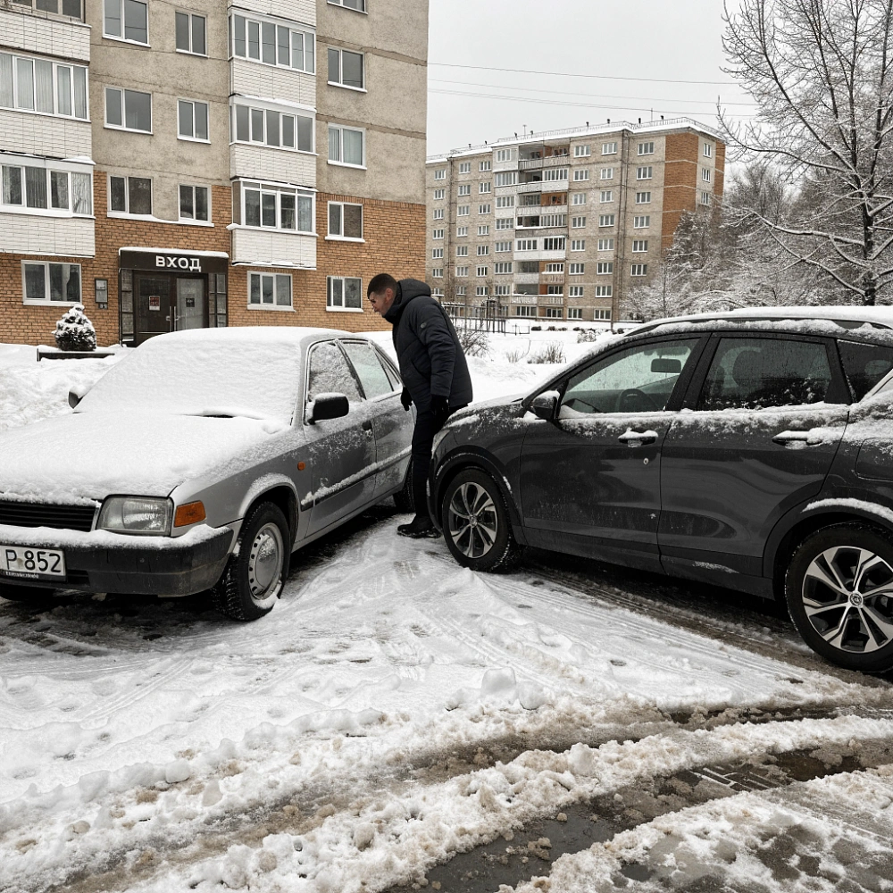 Мужчина сравнивает серебристый седан и кроссовер в заснеженном дворе