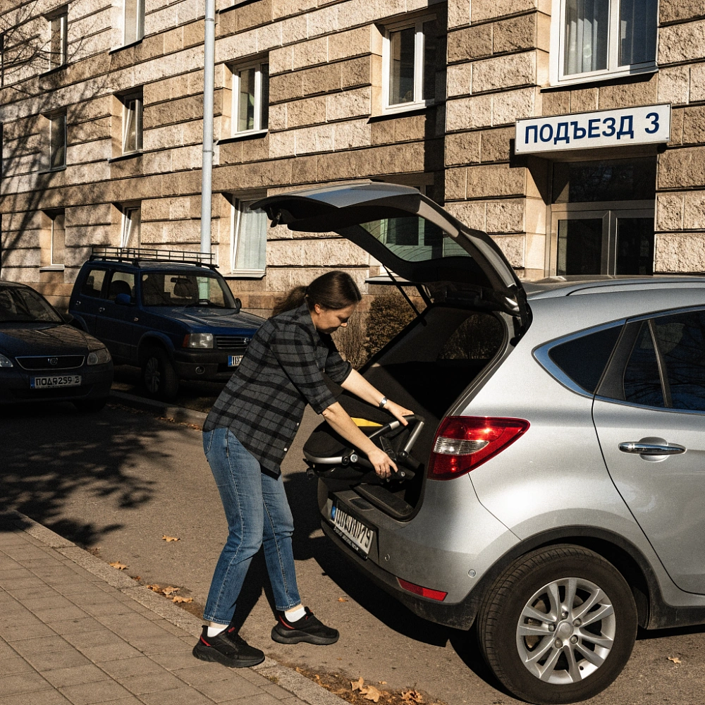 Женщина укладывает сложенную детскую коляску в багажник кроссовера