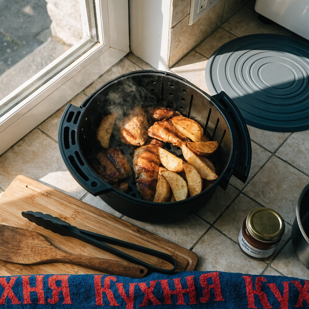 Открытая корзина аэрогриля с картофельными дольками и кусочками курицы
