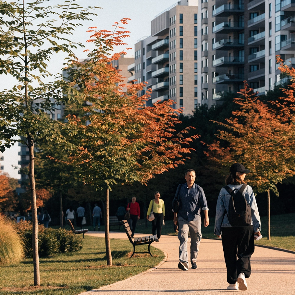 Люди гуляют по дорожке осеннего парка среди современных домов